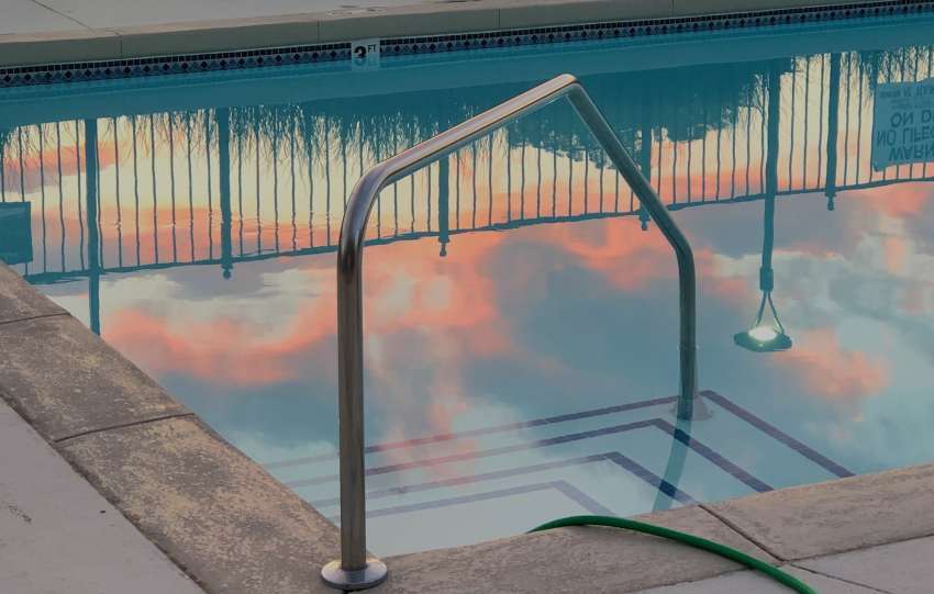 Empty small swimming pool with metal handrail and hose in backyard next to fence in evening